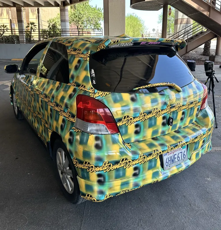 A 2009 Toyota Yaris covered in an AI-generated adversarial pattern parked during a live counter-detection test at Def Con in Las Vegas