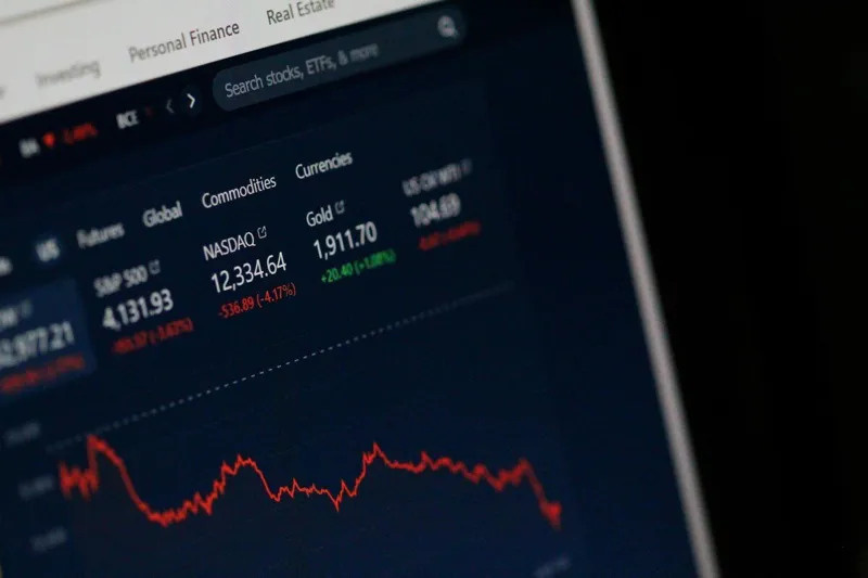 Екран комп'ютера з фінансовими даними про фондові індекси S&P 500 та NASDAQ із червоною лінією графіка падіння.