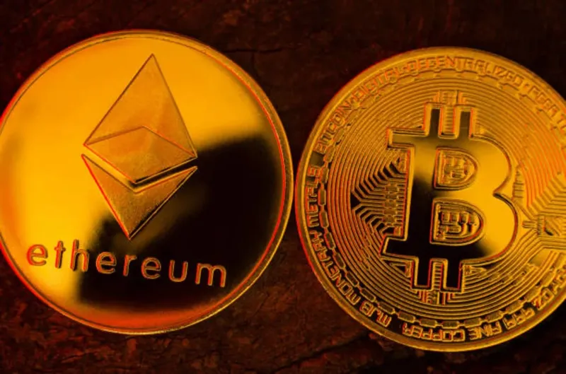 Дві золоті криптовалютні монети — Bitcoin та Ethereum — розташовані поруч на темній поверхні.