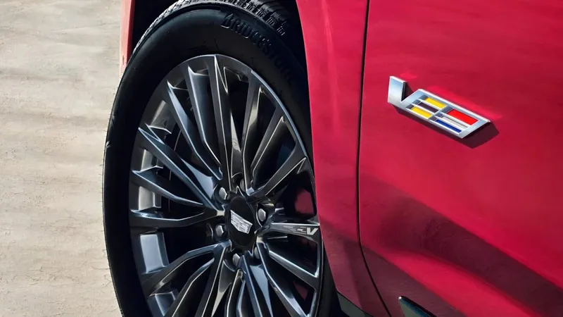 Макрофотографія боку червоного люксового SUV із багатоспицевим колесом і фірмовим значком "V".
