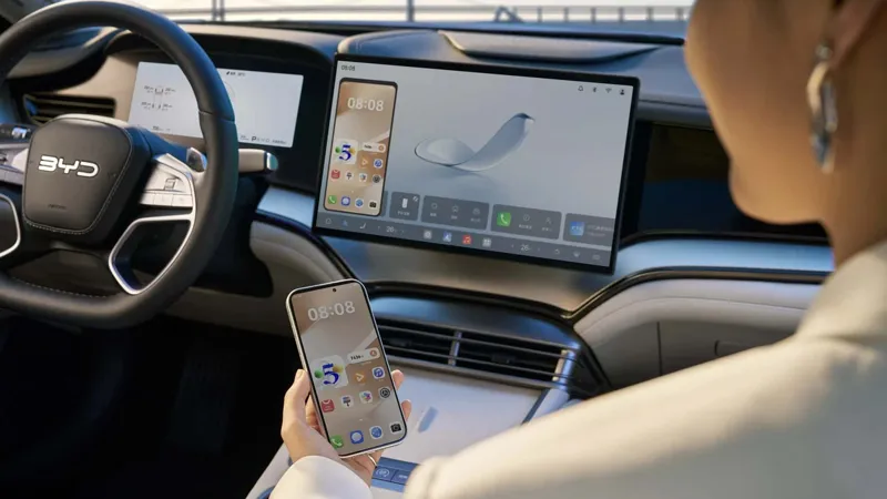 Пасажирка тримає смартфон у салоні сучасного електромобіля BYD, екран якого синхронізований із великим мультимедійним дисплеєм.