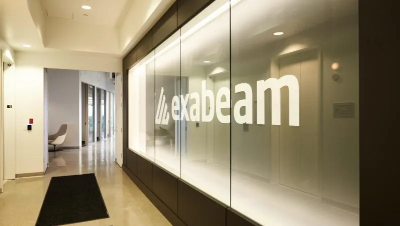 Сучасний вестибюль офісу з великим білим логотипом exabeam на матовому скляному фасаді та яскравим освітленням коридору.