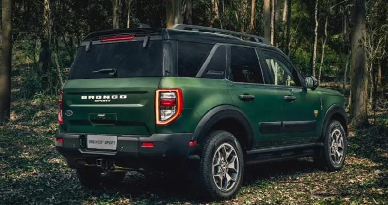 Темно-зелений позашляховик Ford Bronco Sport на тлі густого лісу серед дерев і природної рослинності.