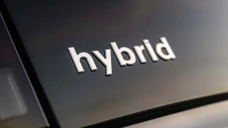 Хромований напиς "hybrid" на чорній панелі кузова сучасного автомобіля з відблисками світла.
