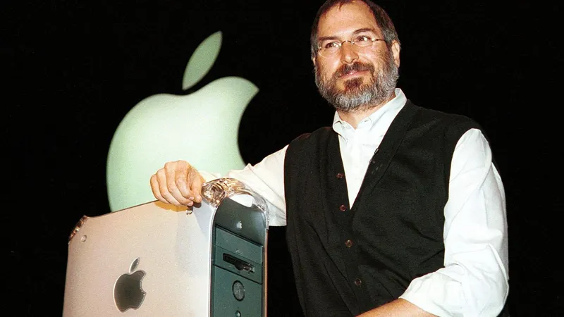 Стів Джобс презентує новий комп'ютер Power Mac G4 на сцені з великим логотипом Apple на фоні.