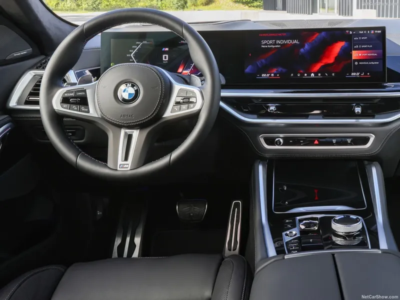 Інтерєр сучасного автомобіля BMW з великими цифровими екранами мультимедіа та спортивним кермом у шкіряній обшивці.