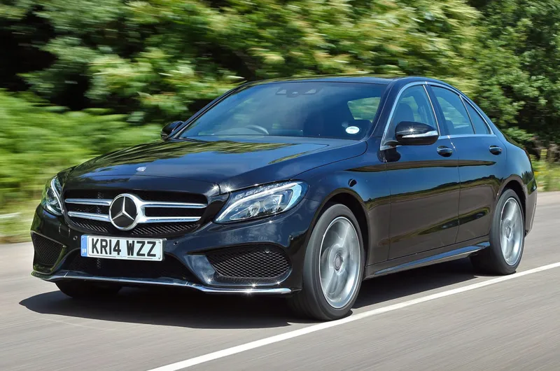 Елегантний чорний Mercedes-Benz C-Class рухається по асфальтованій дорозі на тлі зеленого лісового ландшафту.