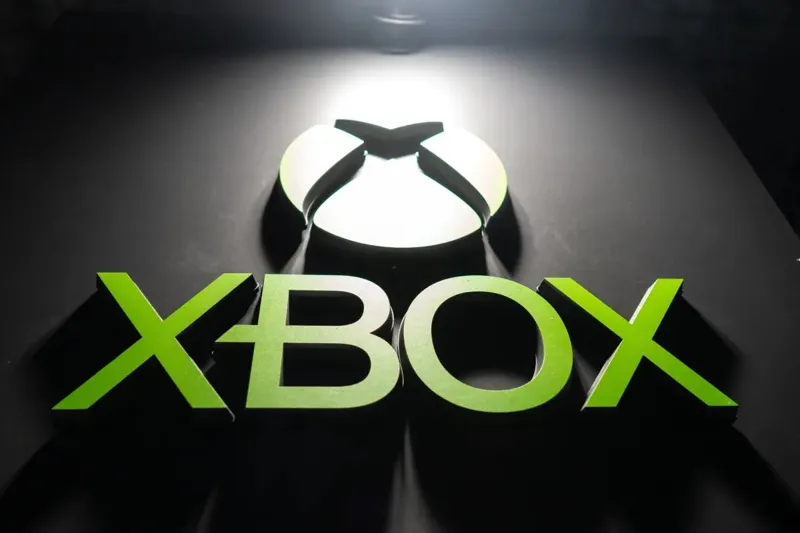 Об'ємний логотип Xbox із написом нижче розміщений на чорному фоні та освітлений яскравим промінням зверху.