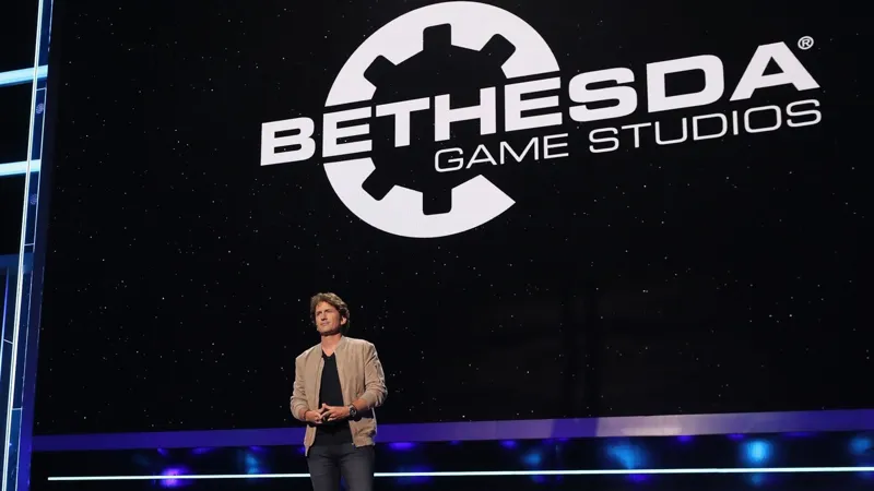 Чоловік у бежевій куртці стоїть на сцені перед великим логотипом Bethesda Game Studios на фоні нічного неба зірок.