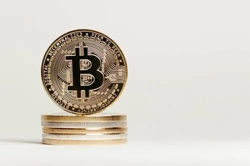 Висока золота монета з символом Біткоїн встановлена вертикально на стопці менших монет на чистому білому фоні.