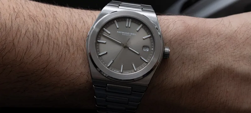 Чоловіче зап'ястя у стильному серебристому годиннику Raymond Weil з металевим інтегрованим браслетом.