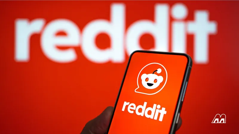 Смартфон у руці з відкритим додатком Reddit на тлі великого білого логотипу платформи на яскраво-червоному фоні.