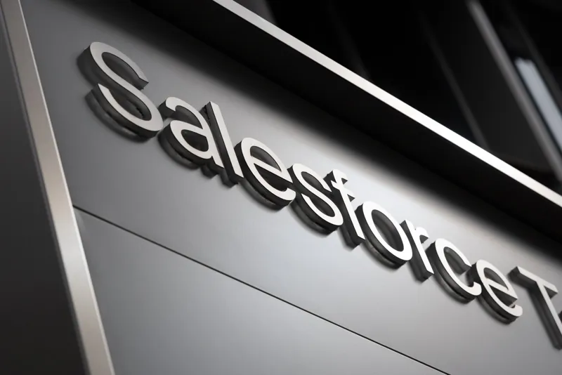 Об’ємний металевий логотип компанії Salesforce розміщено крупним планом на сірій панелі у стилі сучасного корпоративного дизайну.