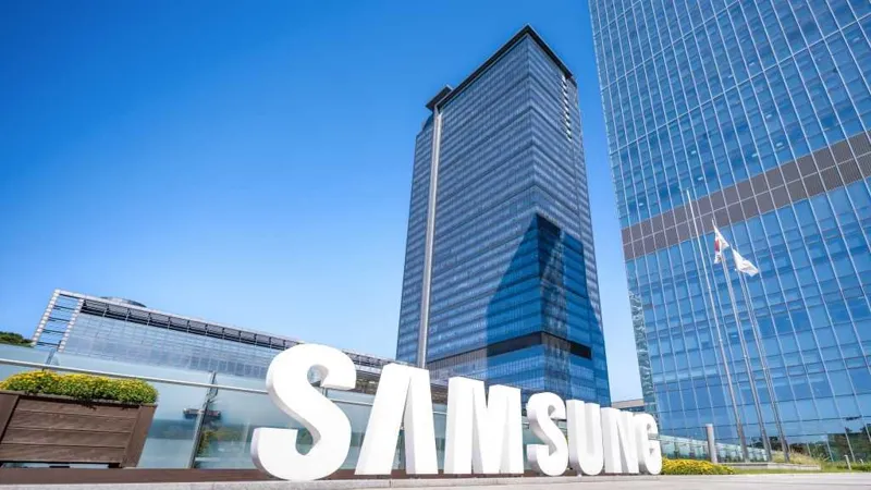 Білий логотип SAMSUNG на фоні сучасних скляних офісних будівель під яскраво-синім небом.