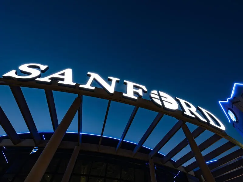 Світлова вивіска SANFORD на фасаді сучасного медичного центру з синьою підсвіткою та металевими конструкціями ввечері.