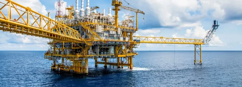 Жовта промислова морська платформа для видобутку енергоресурсів у відкритому морі на фоні яскравого неба з білими хмарами.