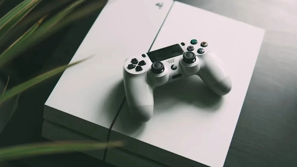 Геймер тримає геймпад консолі PlayStation на тлі ігрового дисплея