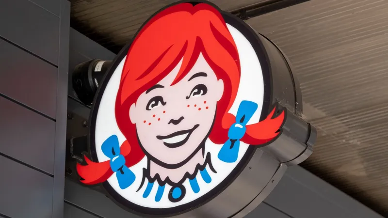 Стилізований маскот Wendy's: усміхнена жінка з рудим волоссям та синіми елементами, розміщений на темній конструкції.